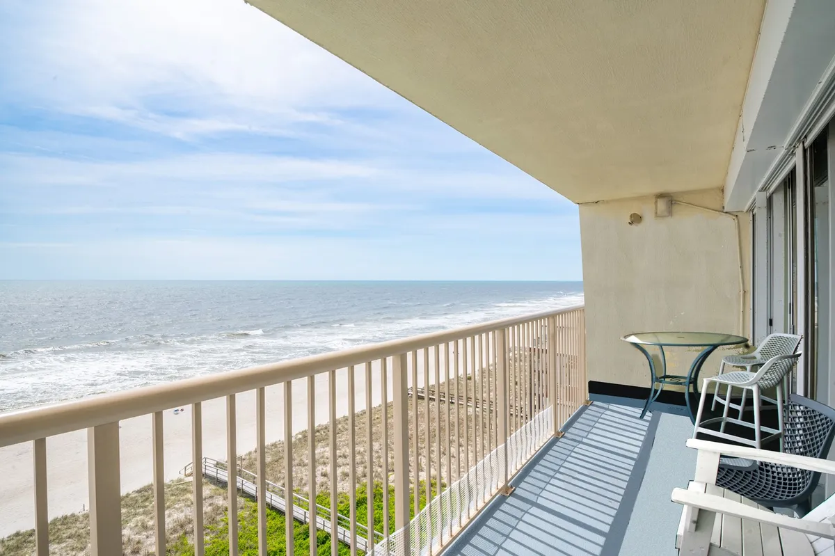 The image showcases the condo's private balcony overlooking the sparkling Atlantic Ocean, with comfortable outdoor furniture perfect for lounging. The scene is serene, capturing the sweeping shoreline and inviting sunrise light, highlighting the ideal spot for morning coffee or a sunset gathering. The beach is just steps away, promising effortless beachside living.