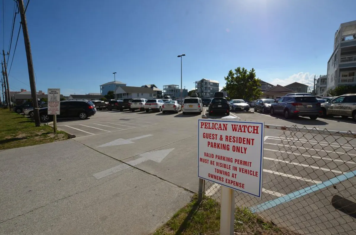 This image displays a dedicated parking area with clearly marked parking sign, several parked cars, and nearby buildings. The exterior setting suggests easy access for guests arriving by vehicle and highlights the convenience of secure, close-by parking.
