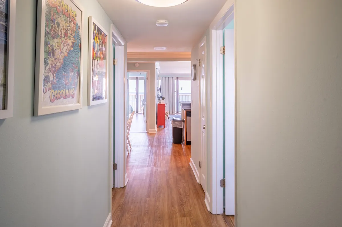A cheerful hallway featuring framed posters, wooden floors, and an open doorway leading to the kitchen. The space feels open and inviting, suggesting easy movement and access.