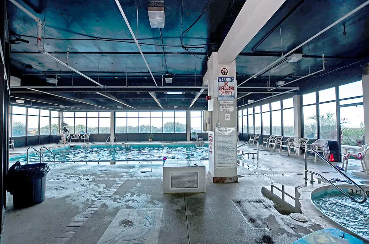 This image captures a brightly-lit indoor swimming pool alongside a hot tub, with large windows letting in natural light and lounge chairs arranged around the water. The setting is tranquil and inviting, suggesting a rejuvenating space for guests to swim or unwind regardless of the season.