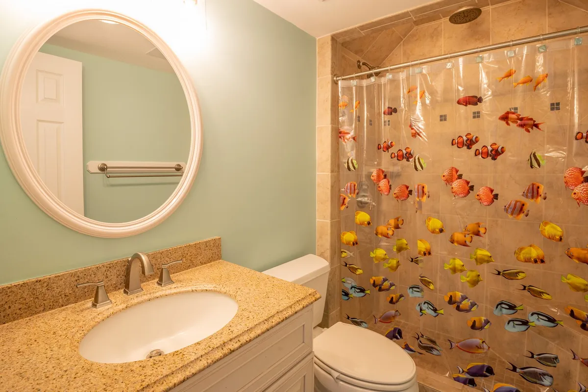 A modern bathroom with a granite countertop, round mirror, and a brightly colored shower curtain, creating a playful yet functional space for the whole family. The setup feels clean and inviting, ideal for post-beach refreshes.