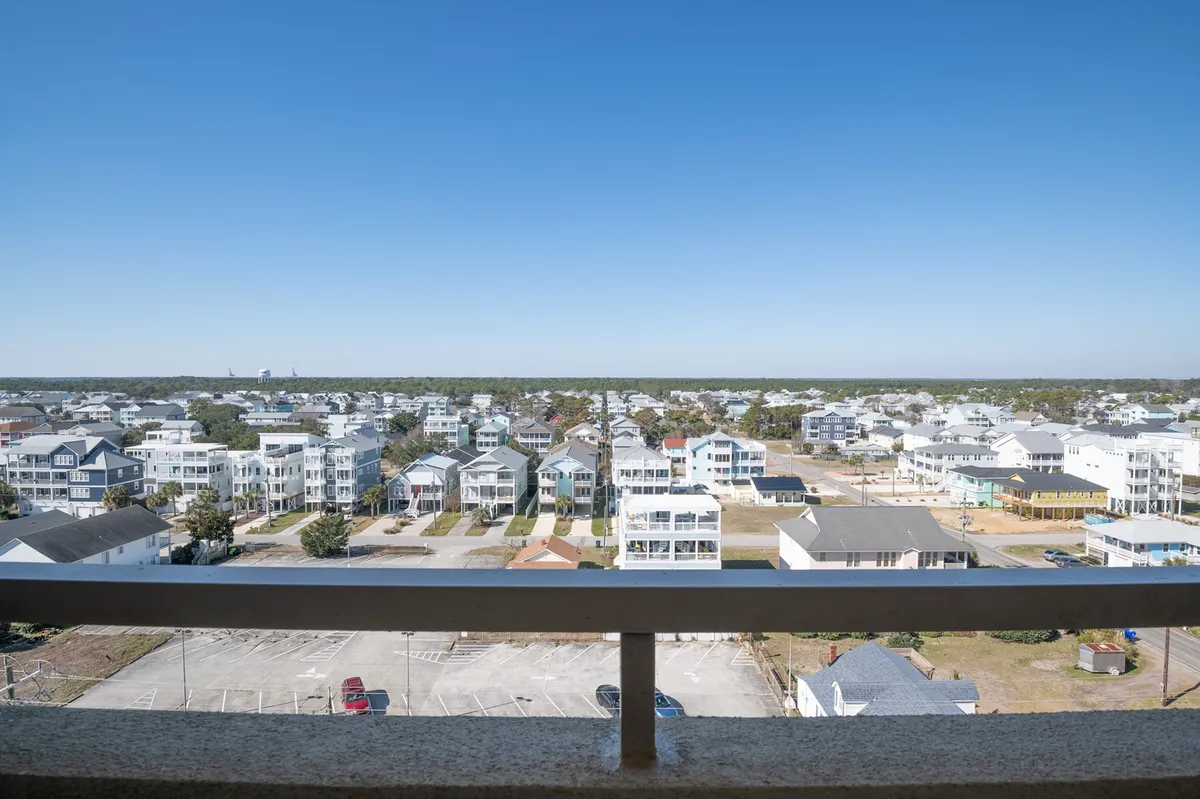 A broad view from the balcony features the neighborhood and ocean horizon, with a clear blue sky overhead. The scene feels open and connected to the local area, offering a glimpse of the vibrant community and making it easy to imagine the short walk to the Tiki Bar and nearby attractions.