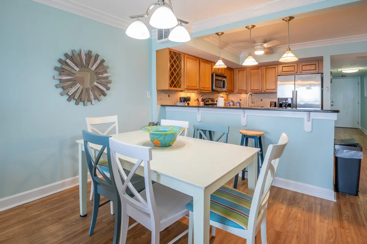 A view of the cheerful dining area with a table set for gathering, a colorful centerpiece, and the adjacent kitchen area visible in the background. The setup invites family meals, board games, or celebration, reinforcing the communal aspect of the space.